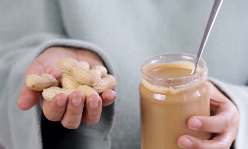 čovek drži u jednoj ruci kikiriki u ljusci a u drugoj teglicu sa kikiriki puterom