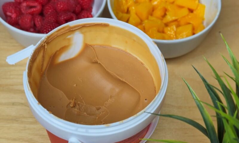 na stolu u činijama maline i mango, pored njih posuda sa kikiriki puterom