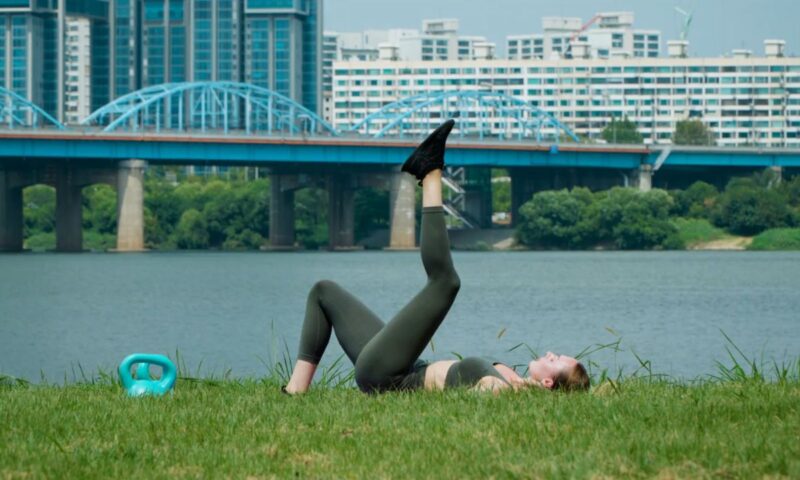 devojka izvodi vežbe za kukove u prirodi, leži na travi i trenira