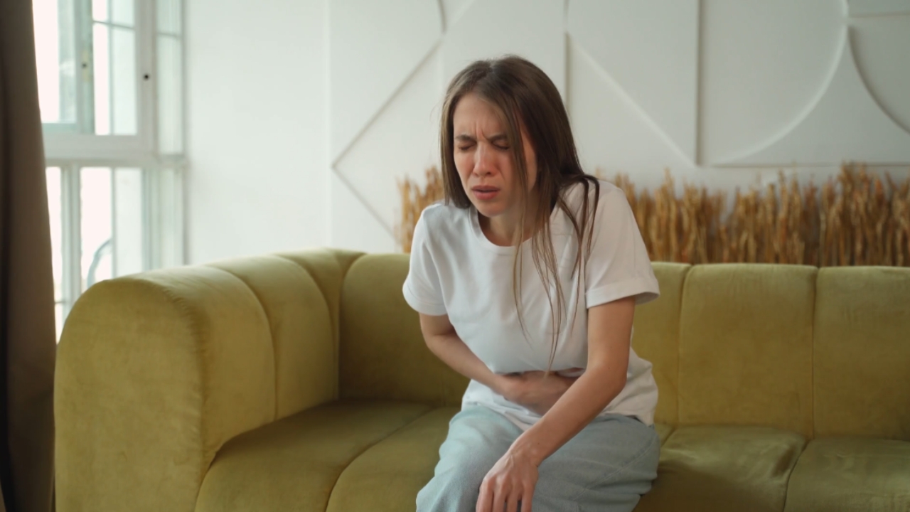 Žena sedi na kauču i drži stomak zbog jakih menstrualnih grčeva